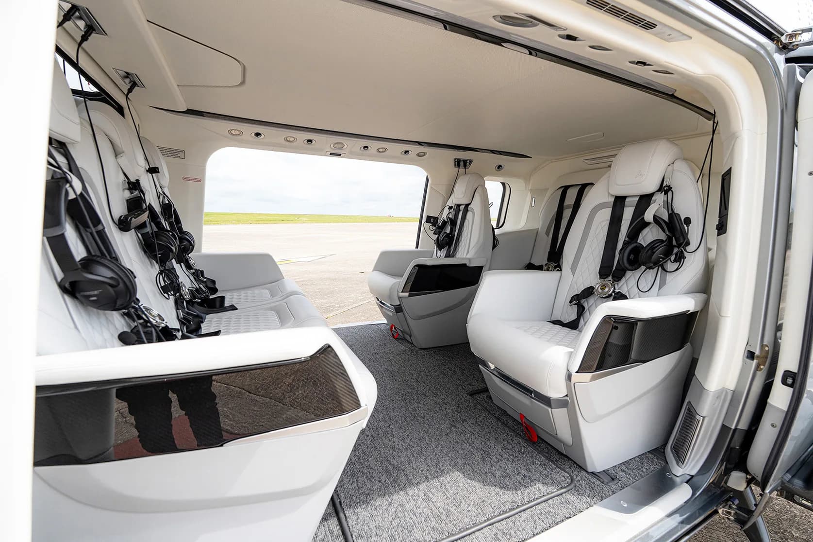 Interior view of the AgustaWestland AW169 helicopter cabin with white leather seats and headsets.