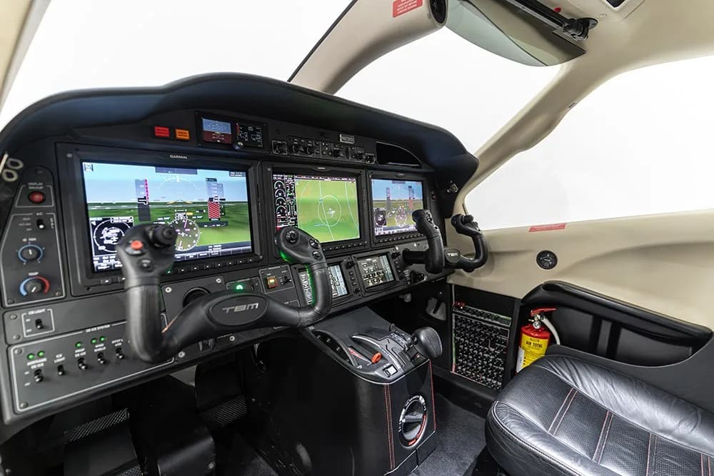 A side view of the TBM 930 cockpit, highlighting the Garmin avionics suite and a fire extinguisher.