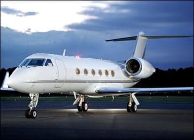 A Gulfstream business jet parked on the tarmac at dusk.