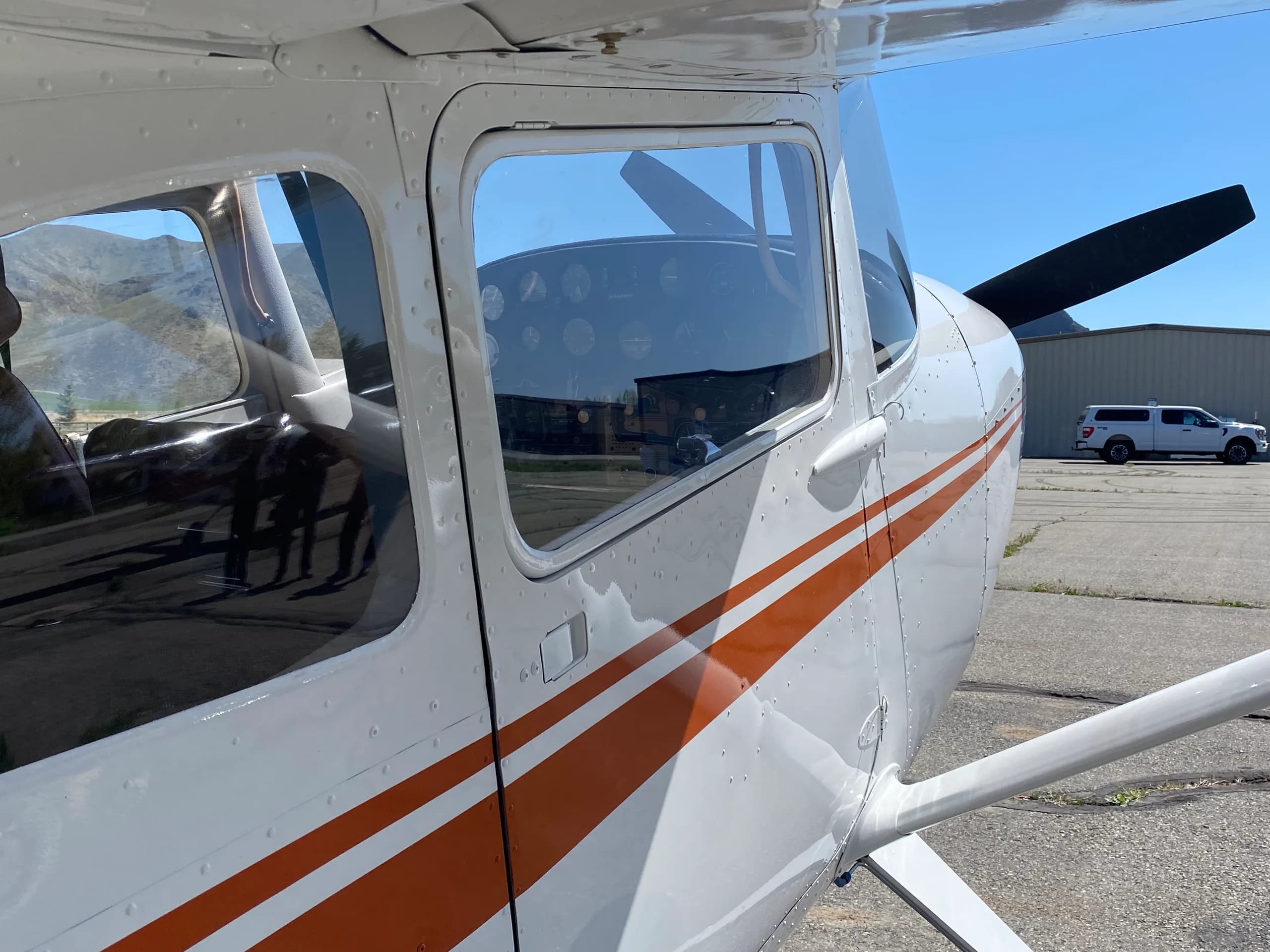 Close-up side view of the front fuselage and propeller of a white Cessna 170B with orange stripes.