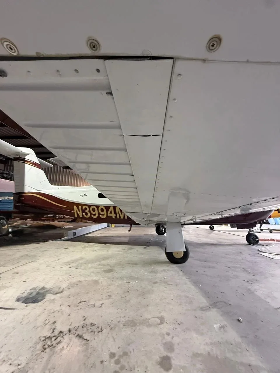 The underside of the wing and landing gear of the Piper Lance II aircraft N3994M, parked in a hangar.