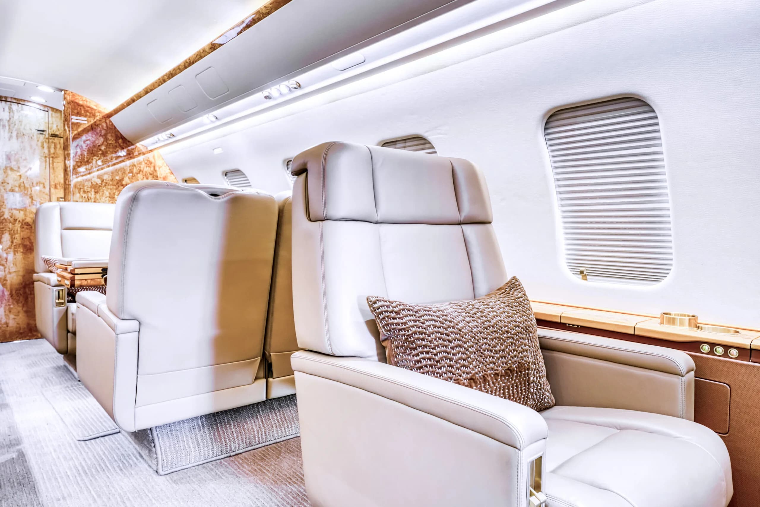 A view of the luxurious cabin interior with light-colored leather seats and a patterned pillow next to a window.