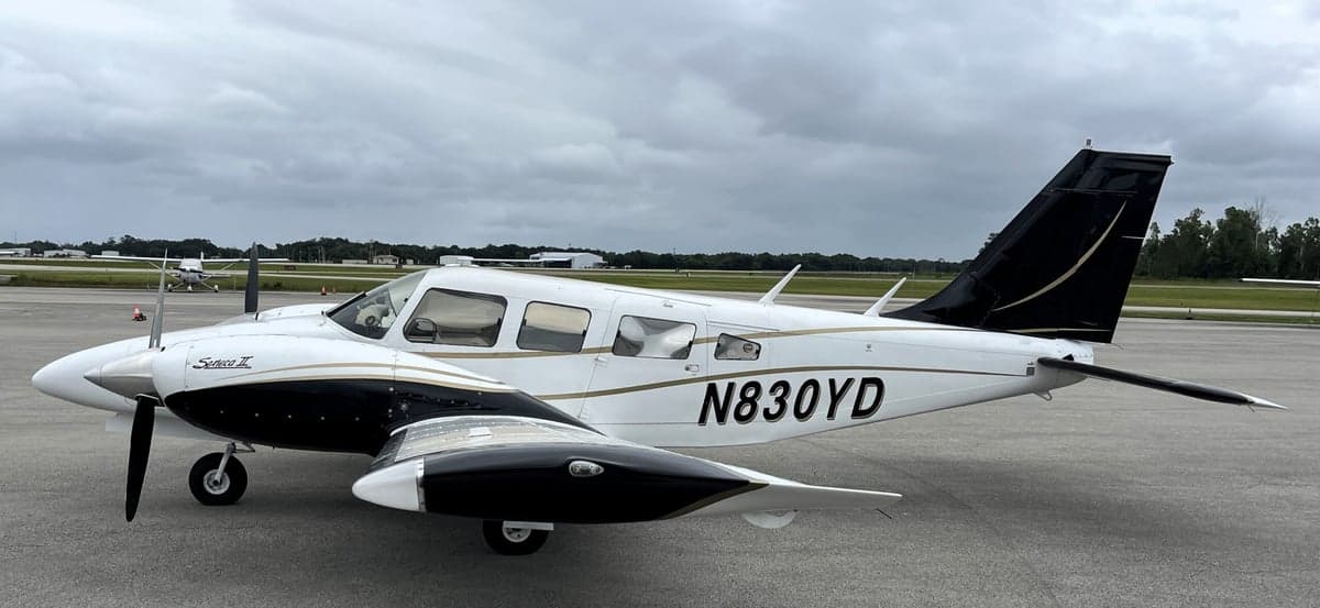 A Piper Seneca II aircraft with a white and black paint scheme is parked on the tarmac.