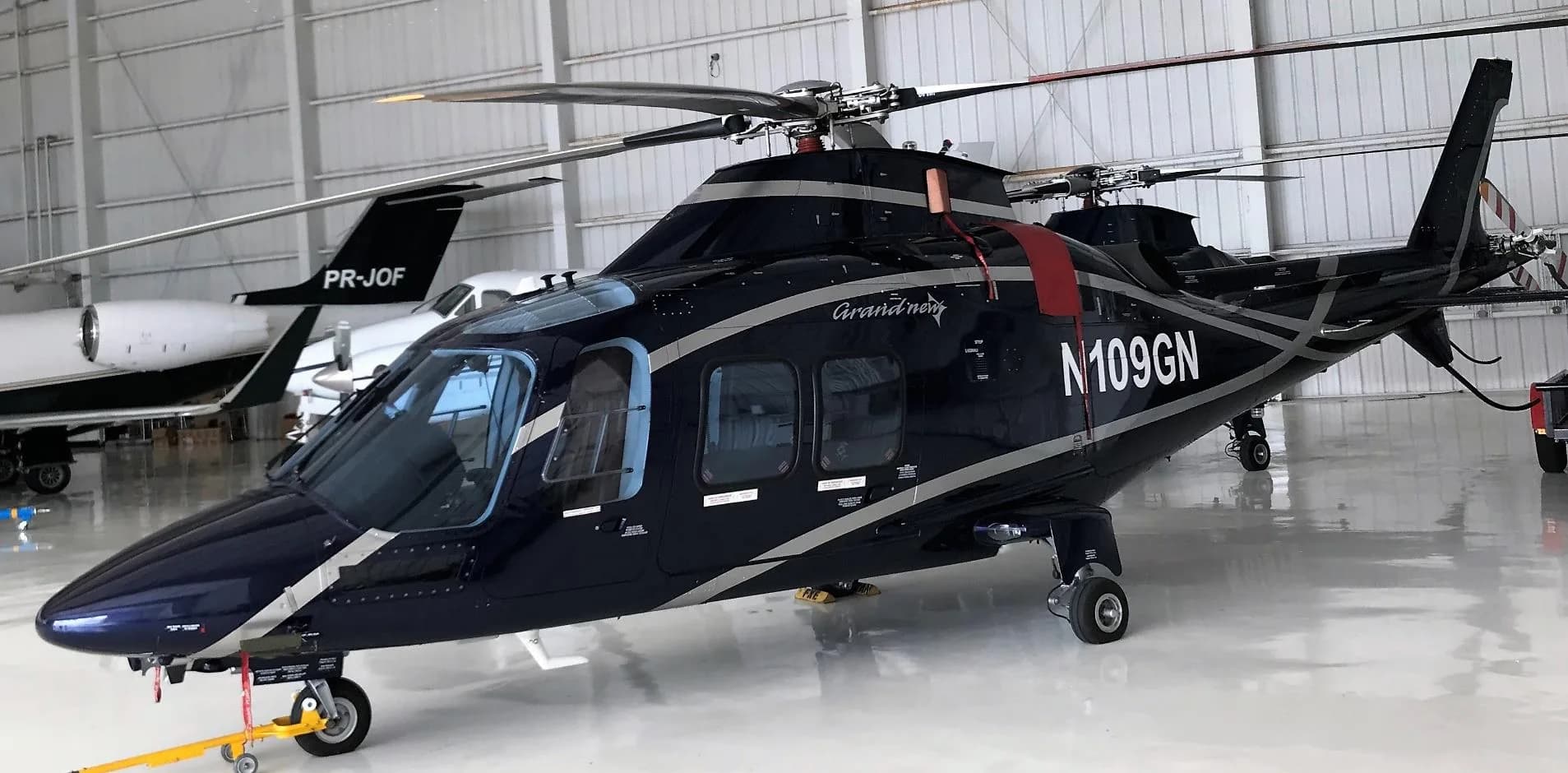 A black AgustaWestland AW109 GrandNew helicopter with registration N109GN inside a hangar.