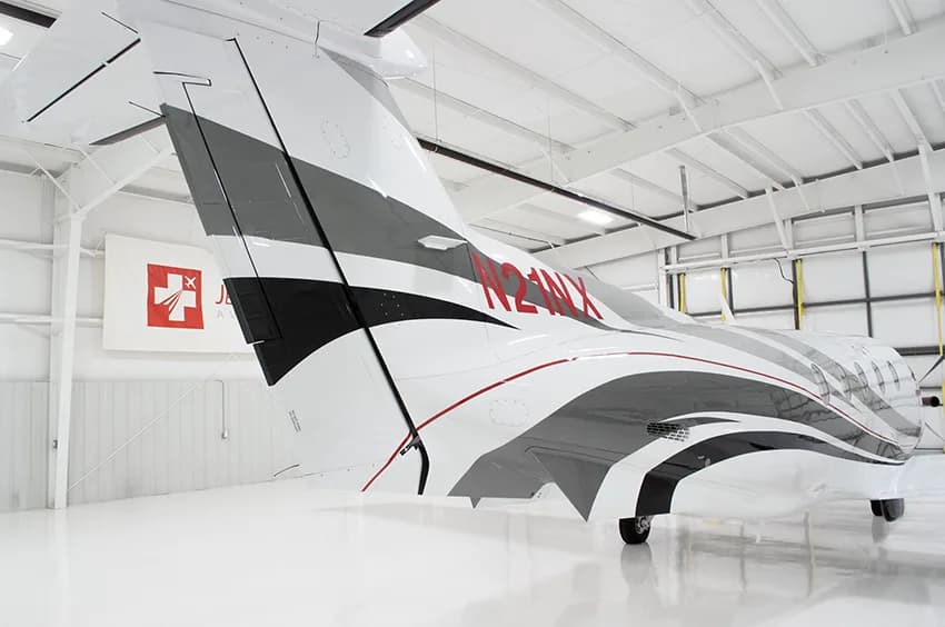 A close-up of the black wingtip with red stripes and the tail of a Pilatus PC-12NG aircraft, showing registration N21NX.
