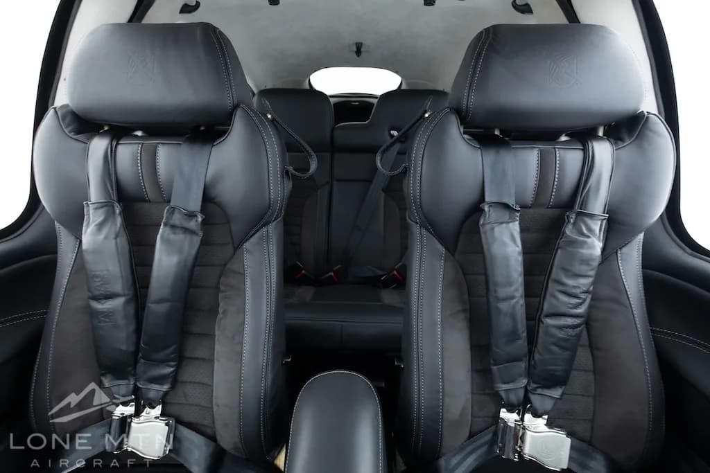 The black leather front seats of a Cirrus SR22 aircraft cabin, showing seatbelts and headrests.