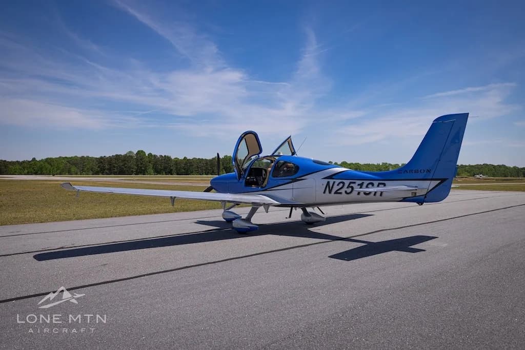 A side view of the blue and silver Cirrus SR20 aircraft (N251SR) with open doors, parked on an airfield.