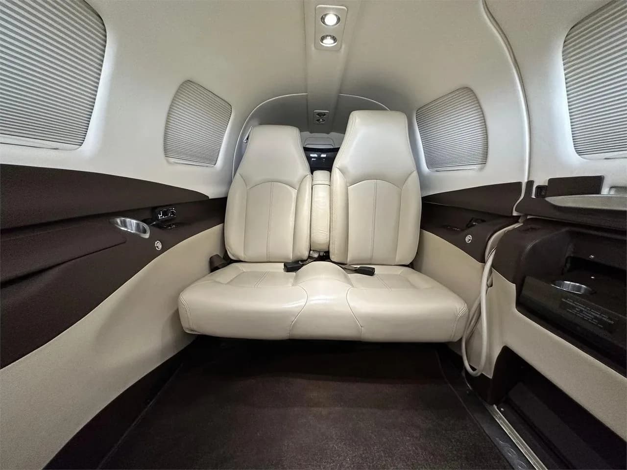 The rear cabin interior of the Piper M350 aircraft, featuring two light-colored leather seats facing forward.