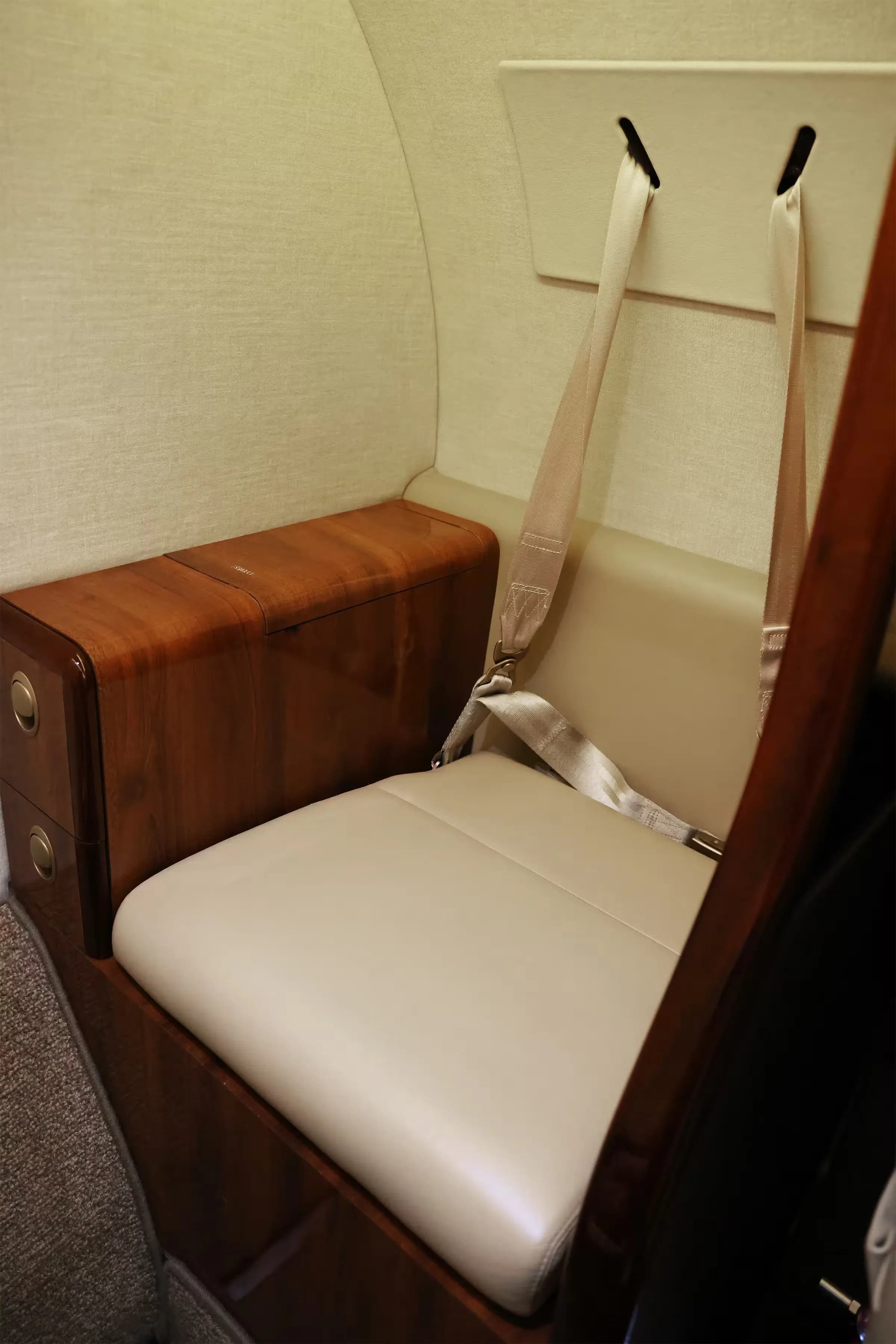 A close-up of a beige leather cabin seat and a wooden side cabinet in the Cessna Citation CJ2+ interior.