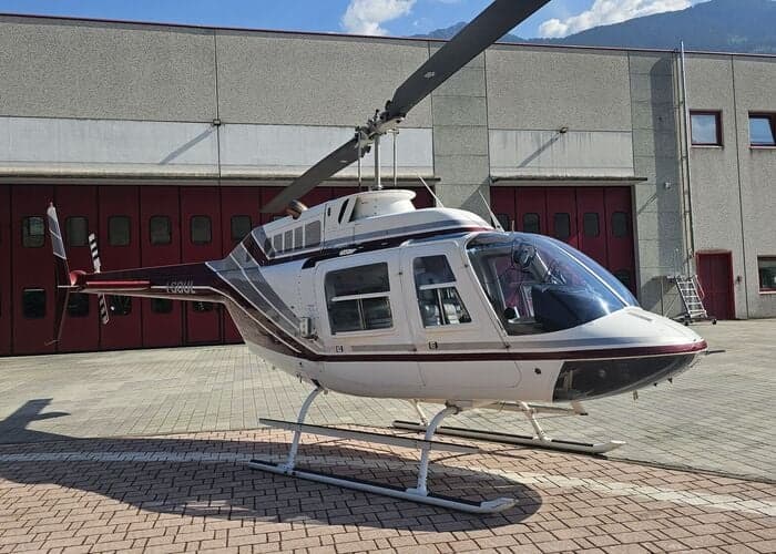 Side view of a white and maroon Bell 407 helicopter parked on a paved surface.