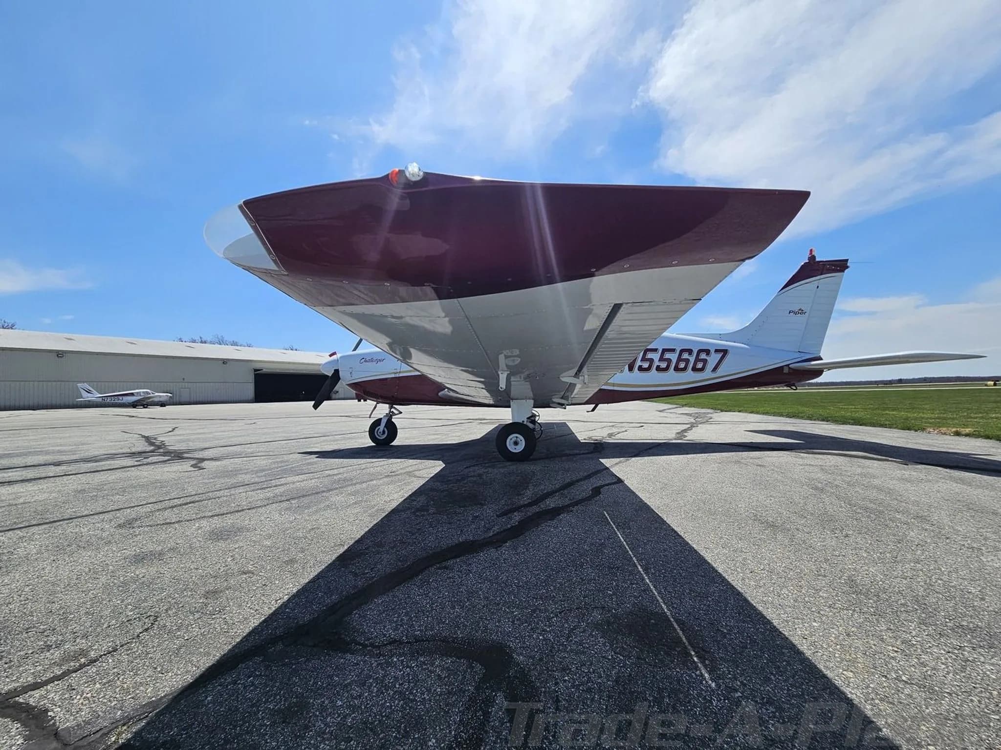 Low-angle side view of a white and maroon Piper PA-28 Challenger aircraft with registration N55667 on an airfield.