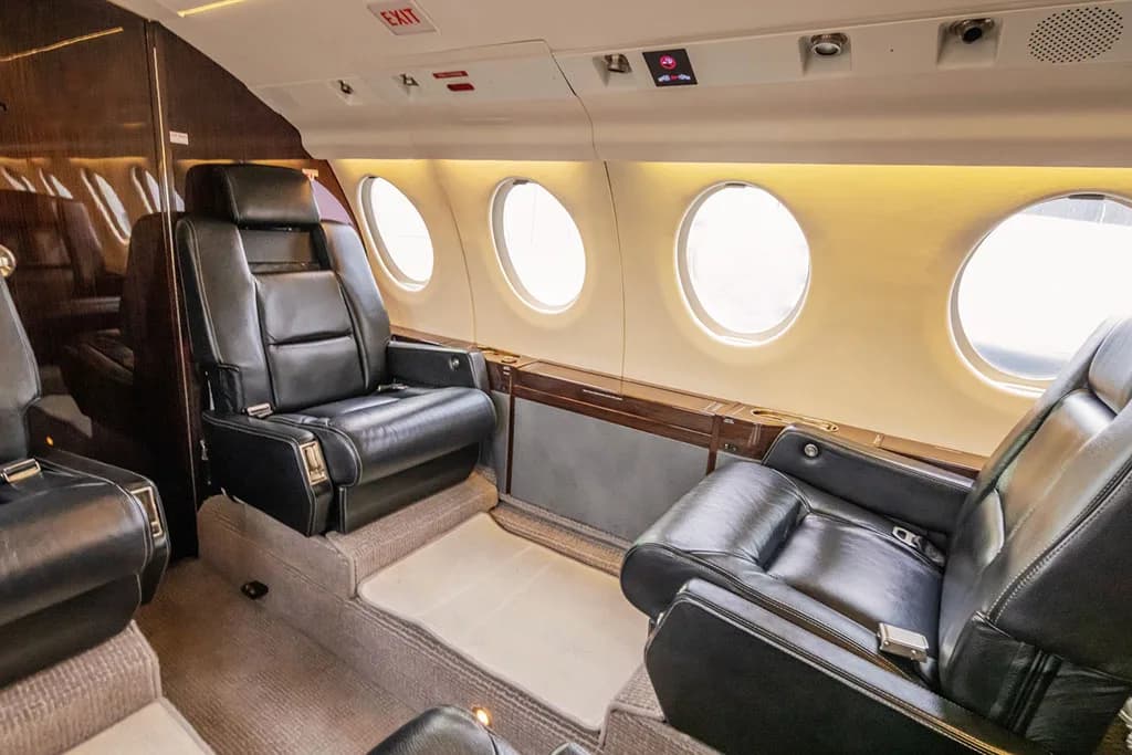 The aircraft's cabin interior with two black leather seats facing each other, next to large oval windows.