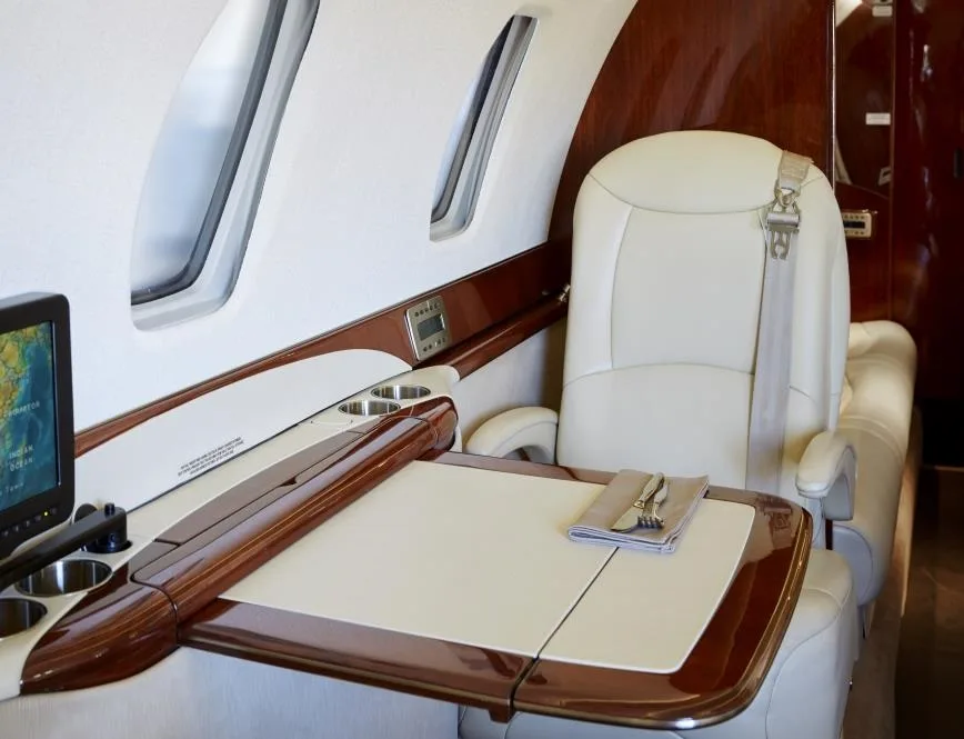 A view of the aircraft interior with a cream-colored leather seat and a table set with silverware.