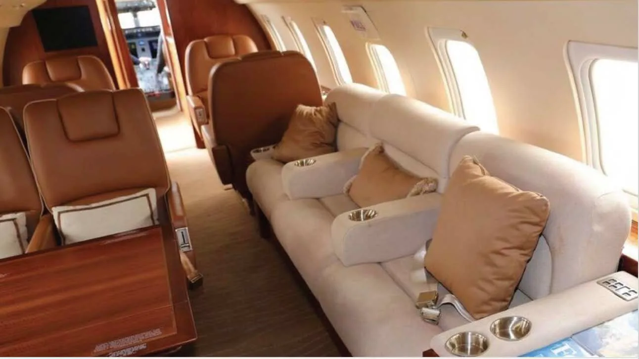 The luxurious interior cabin of a business jet, featuring a beige sofa and tan leather seats.