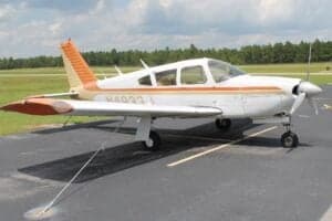 A white and orange Piper PA-28 Cherokee parked on the tarmac.
