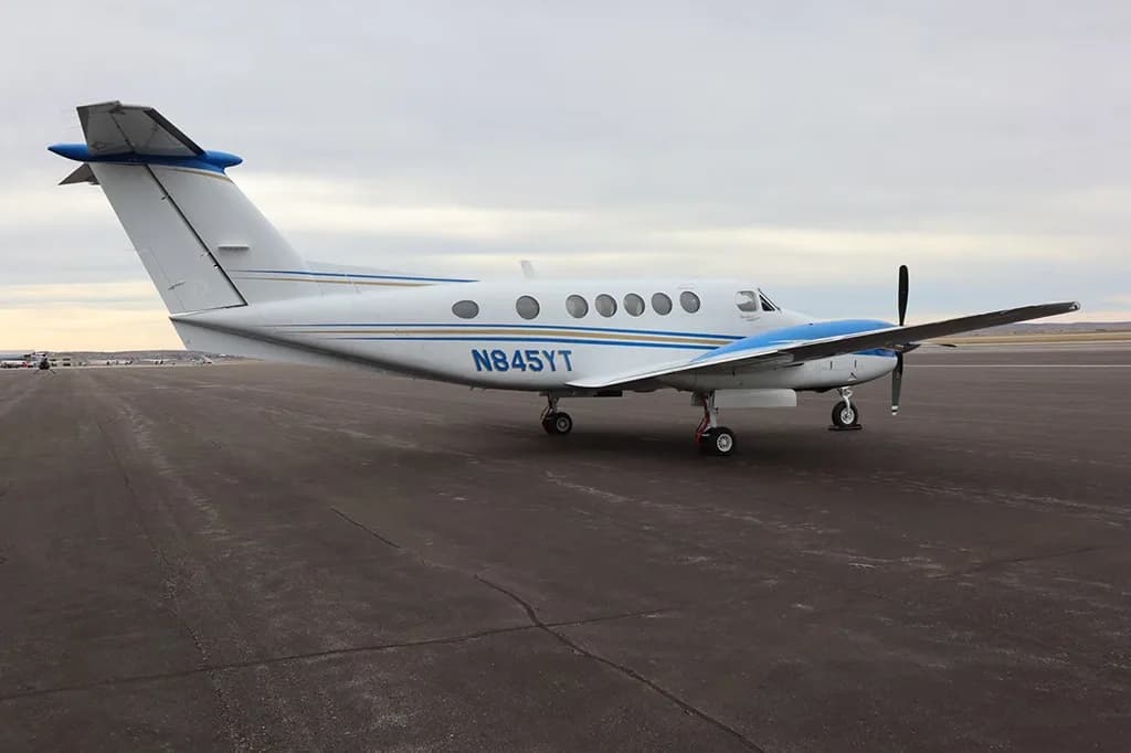 A three-quarter rear view of a white and blue twin-engine turboprop aircraft, N845YT, on an airport runway or tarmac.