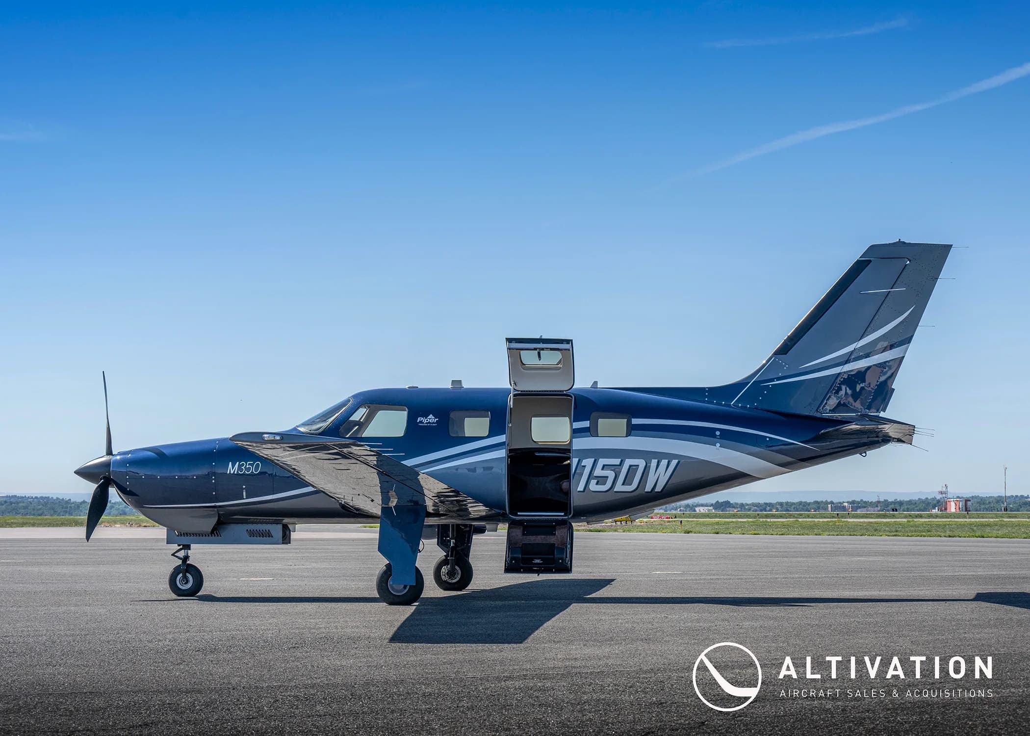 A dark blue Piper M350, tail number N115DW, parked on a tarmac with its main and cargo doors open.