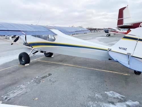A white Super Cub aircraft with blue and yellow stripes and tail number N4108Z, parked on a snowy tarmac.