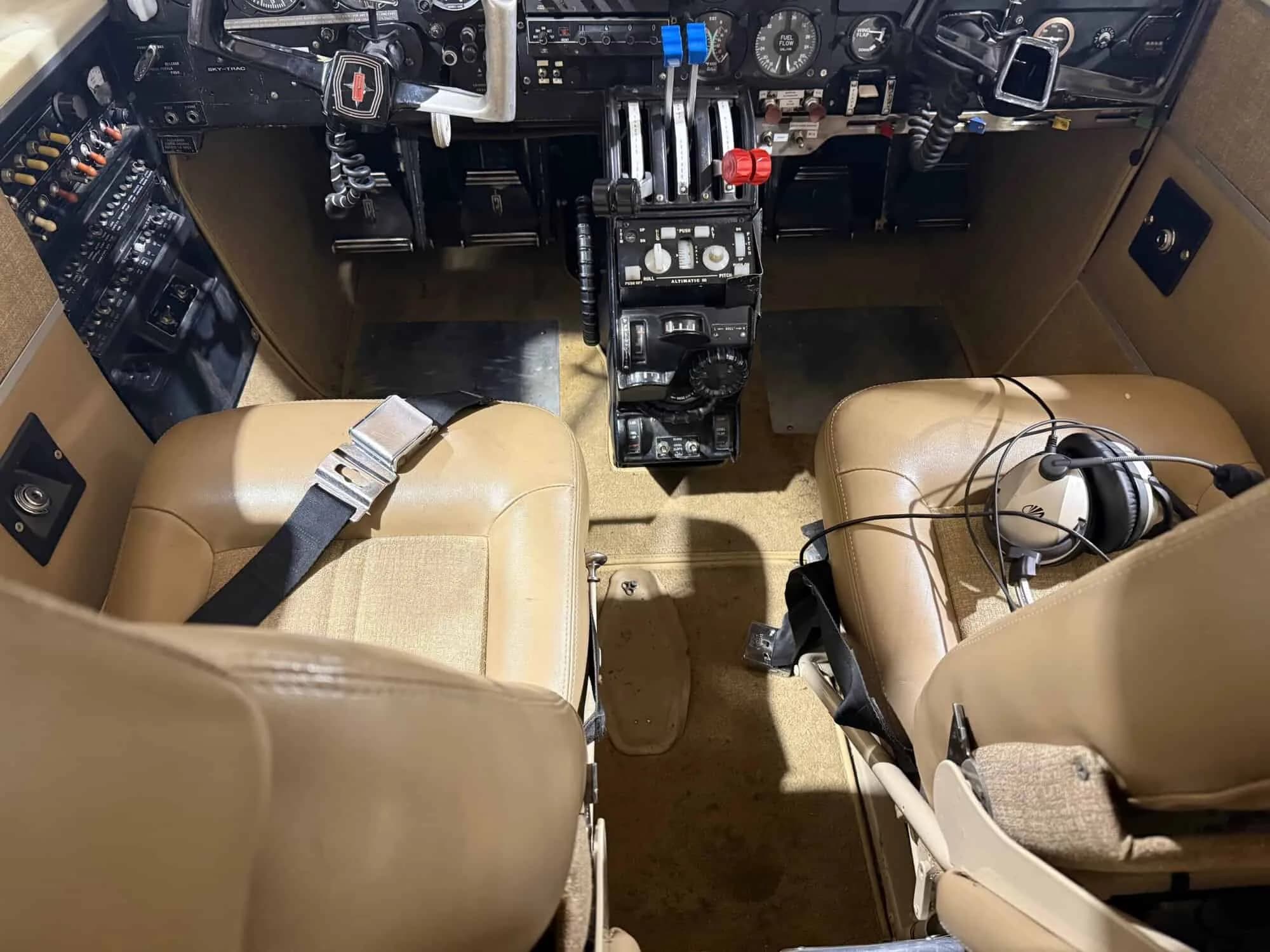 View of the aircraft cockpit from the cabin, showing the instrument panel, controls, and two tan seats.