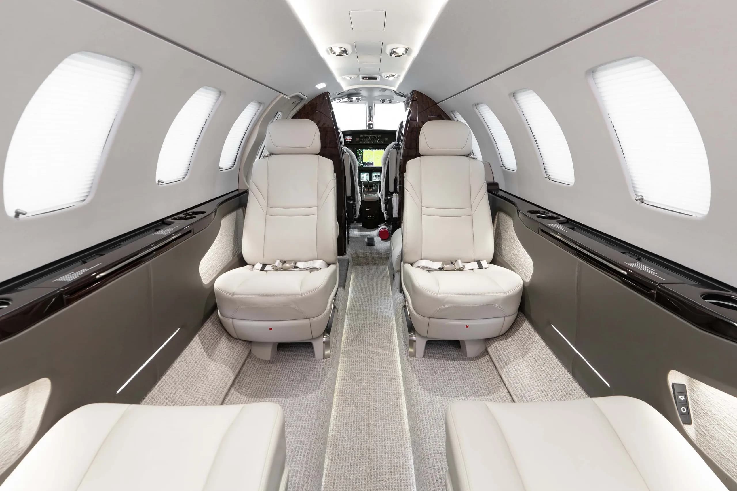 The interior cabin of a business jet with light grey leather seats, looking forward into the cockpit area.