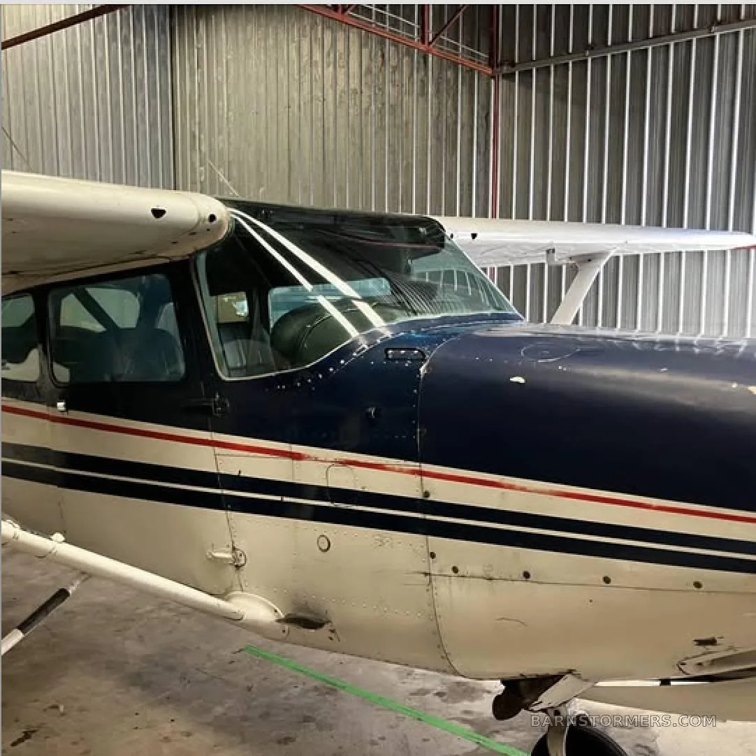 A close-up front-right view of the cockpit and nose of a blue and white aircraft inside a hangar.