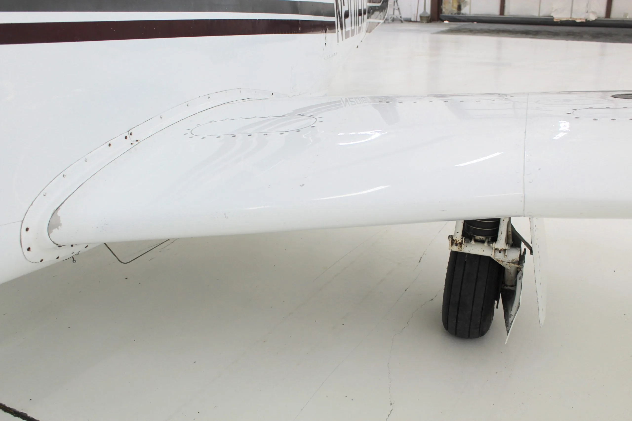 Close up of the wing and landing gear of the white and brown N201BP aircraft in a hangar.
