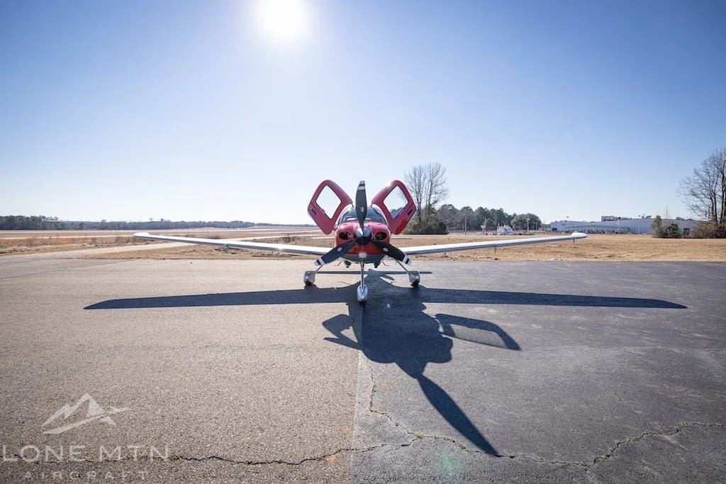 A front view of a red and silver Cirrus SR22T aircraft with open doors parked on an asphalt ramp.