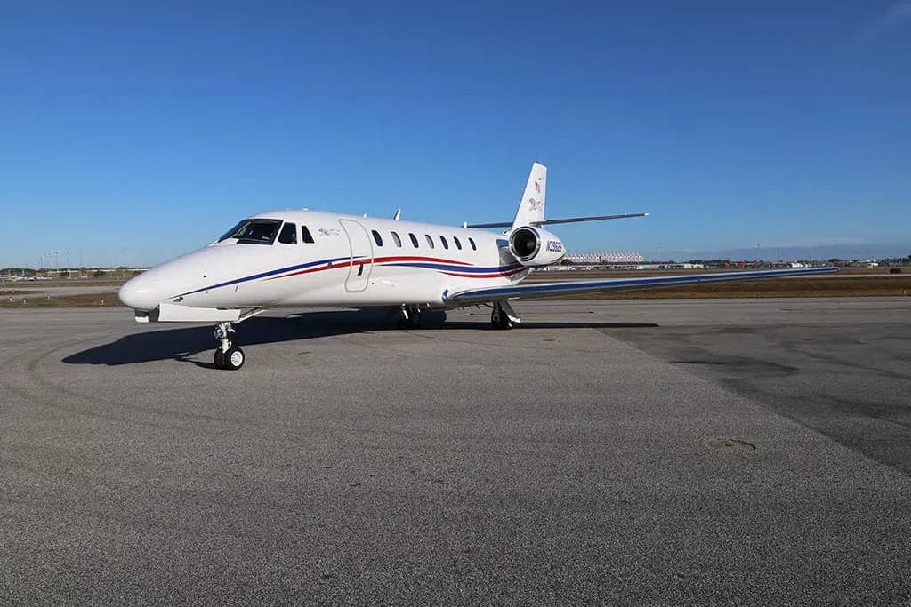 A white Cessna Citation business jet with red and blue stripes and registration N396BB on the tail, parked on an airfield under a clear blue sky.