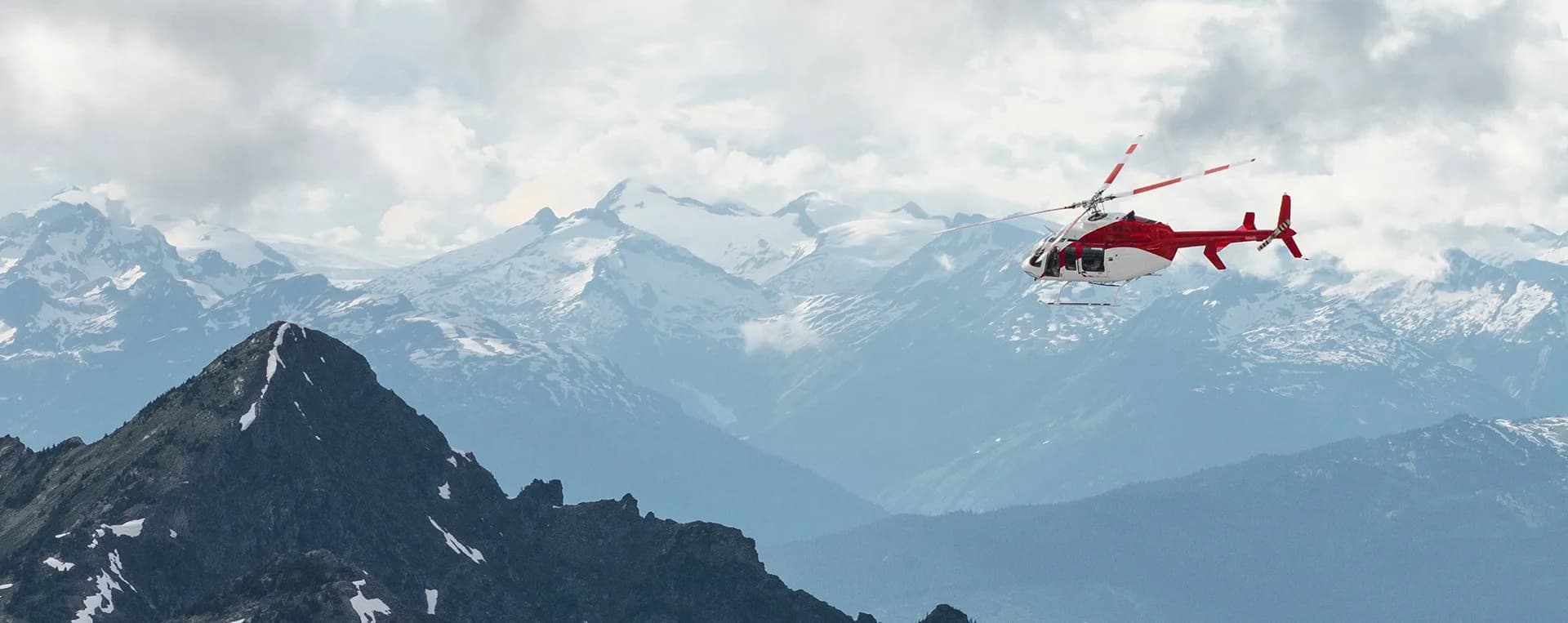 Red and white helicopter flying over mountains.