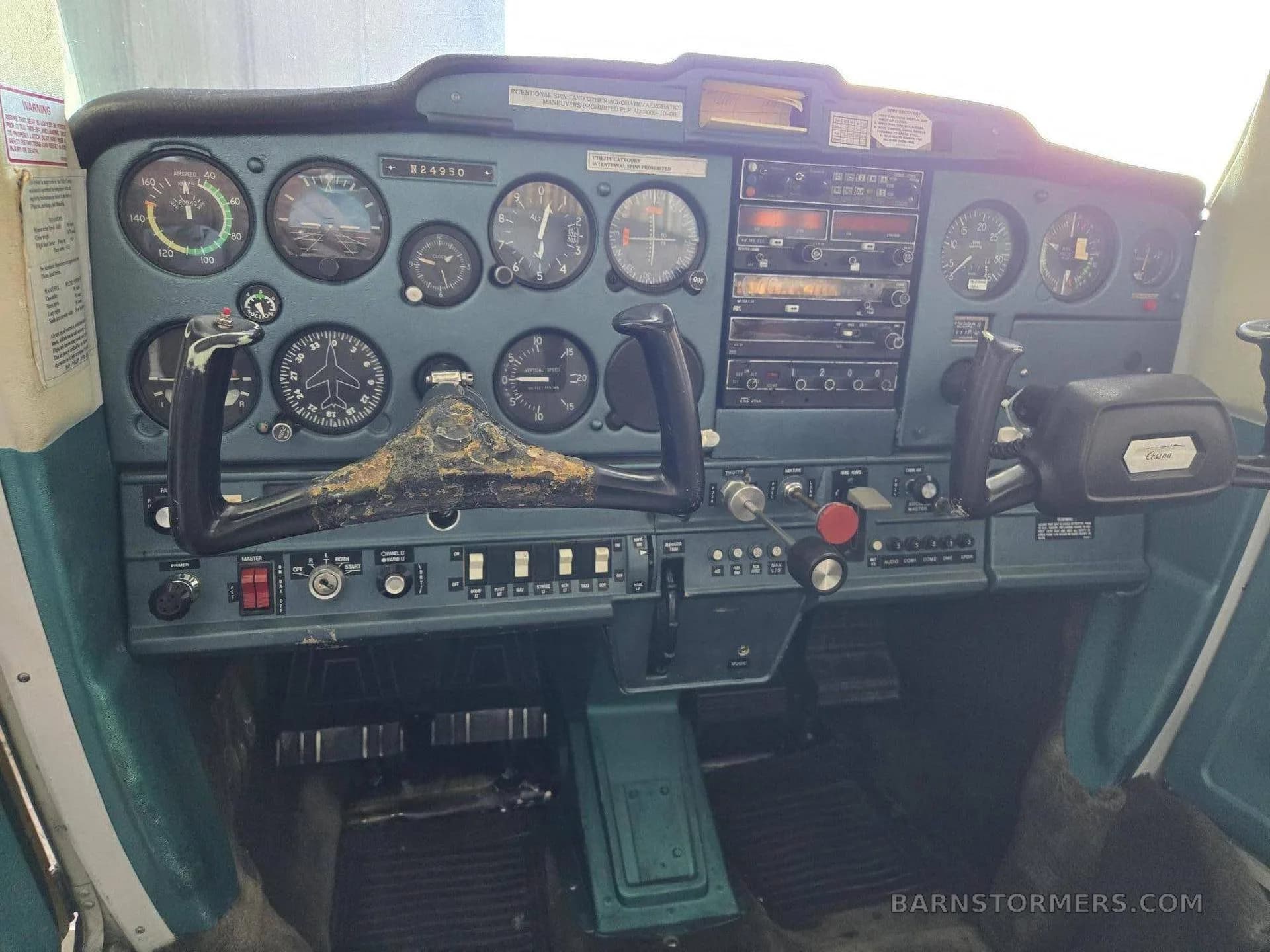 A wider view of the cockpit instrument panel and controls of a light aircraft, showing the worn control yokes and analog gauges.