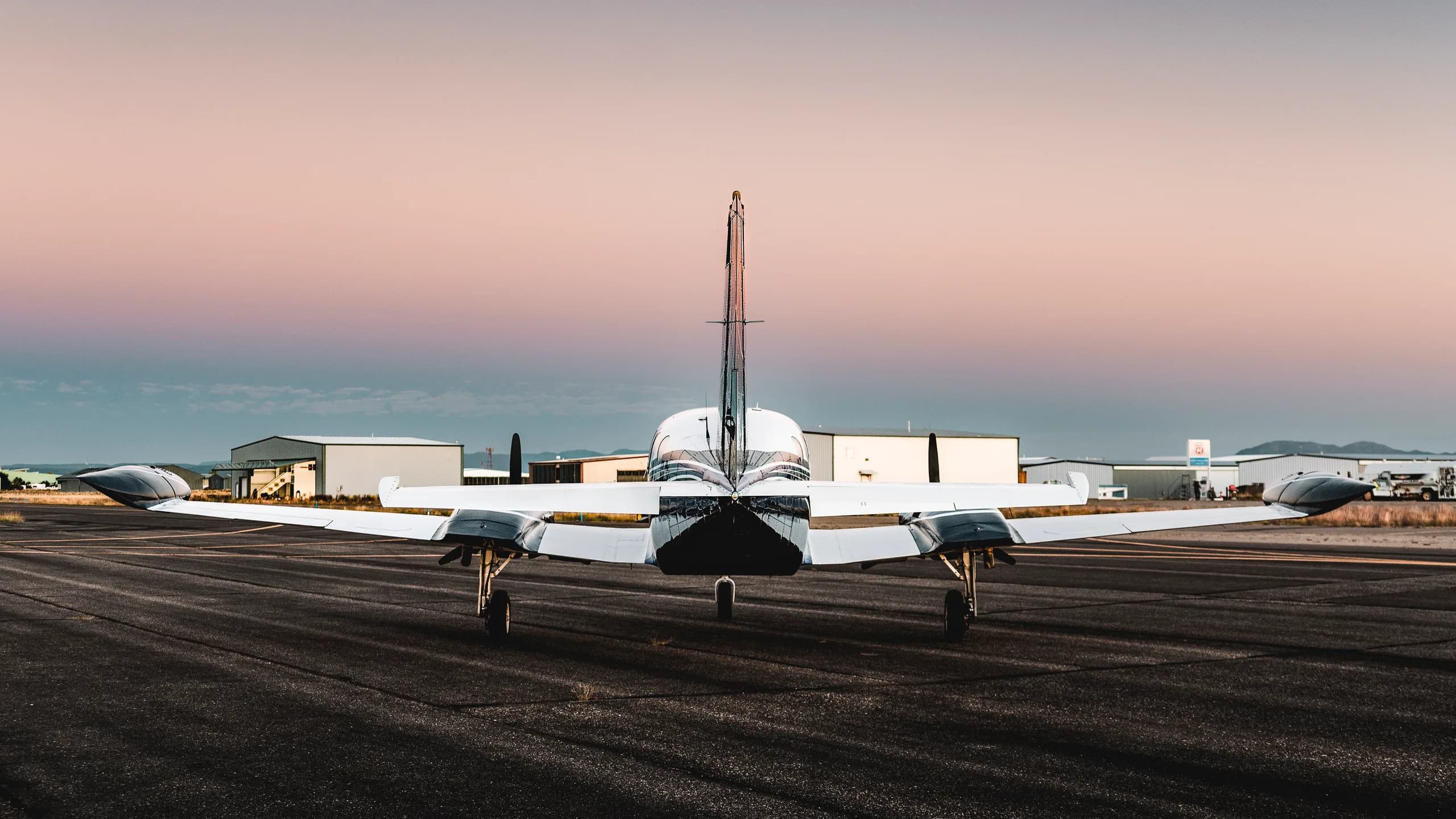 Rear view of a white and blue twin-engine aircraft parked on a runway at sunset.