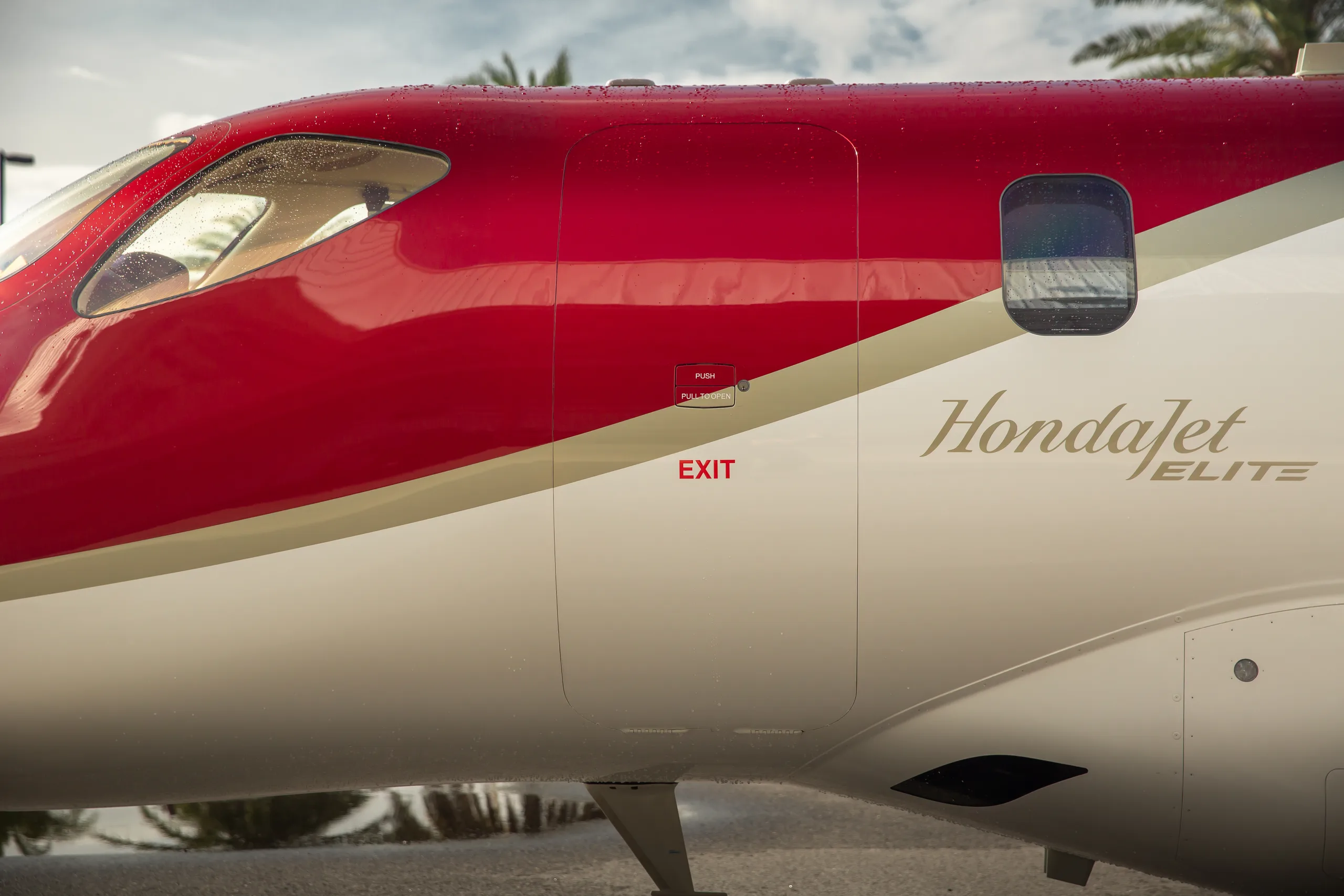 A close-up of the red and white fuselage of a HondaJet, showing the 'HondaJet' script and an 'EXIT' sign.