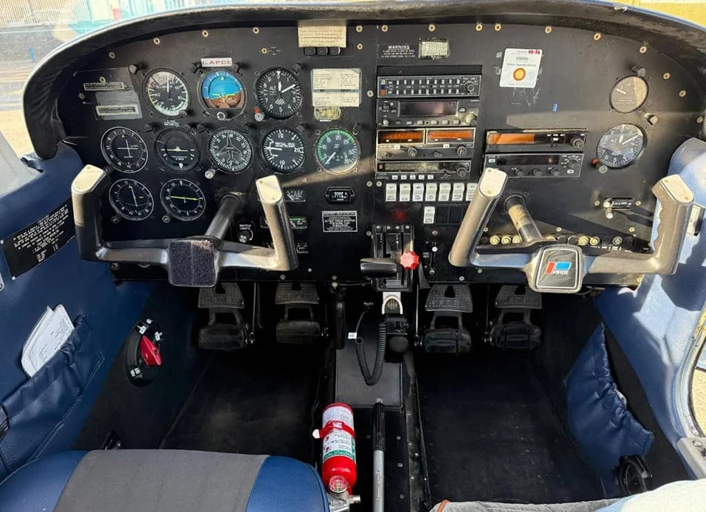 The cockpit of a small aircraft, showing the instrument panel with gauges, radios, and dual control yokes.