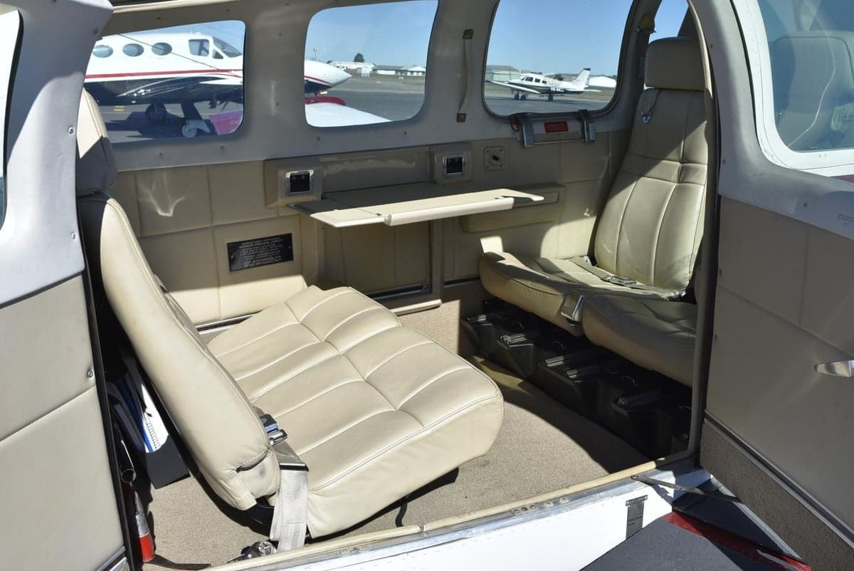 The beige leather interior of a small aircraft cabin with a fold-out table and seats.