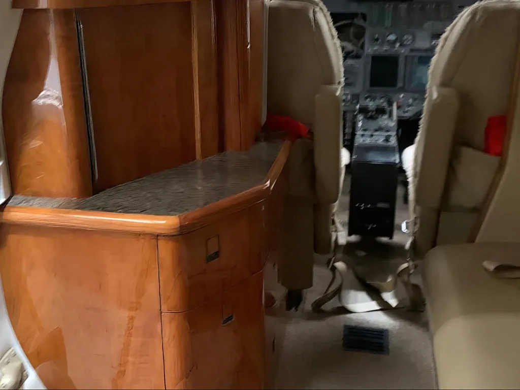 A view of the aircraft's cabin interior, featuring a polished wood cabinet and beige seats in the background.