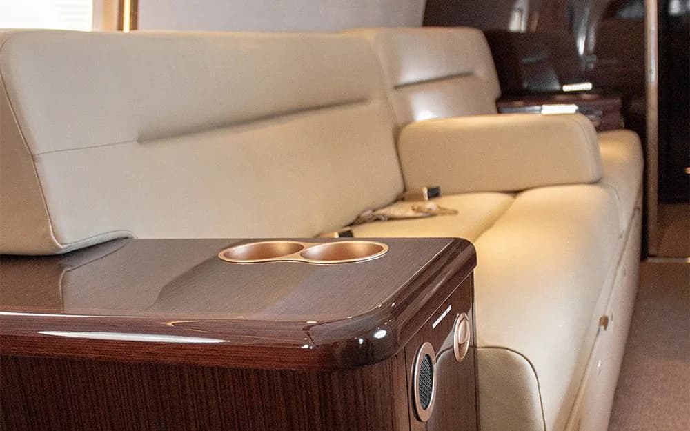 A close-up of a beige leather aircraft sofa with a polished wooden side table featuring cup holders.