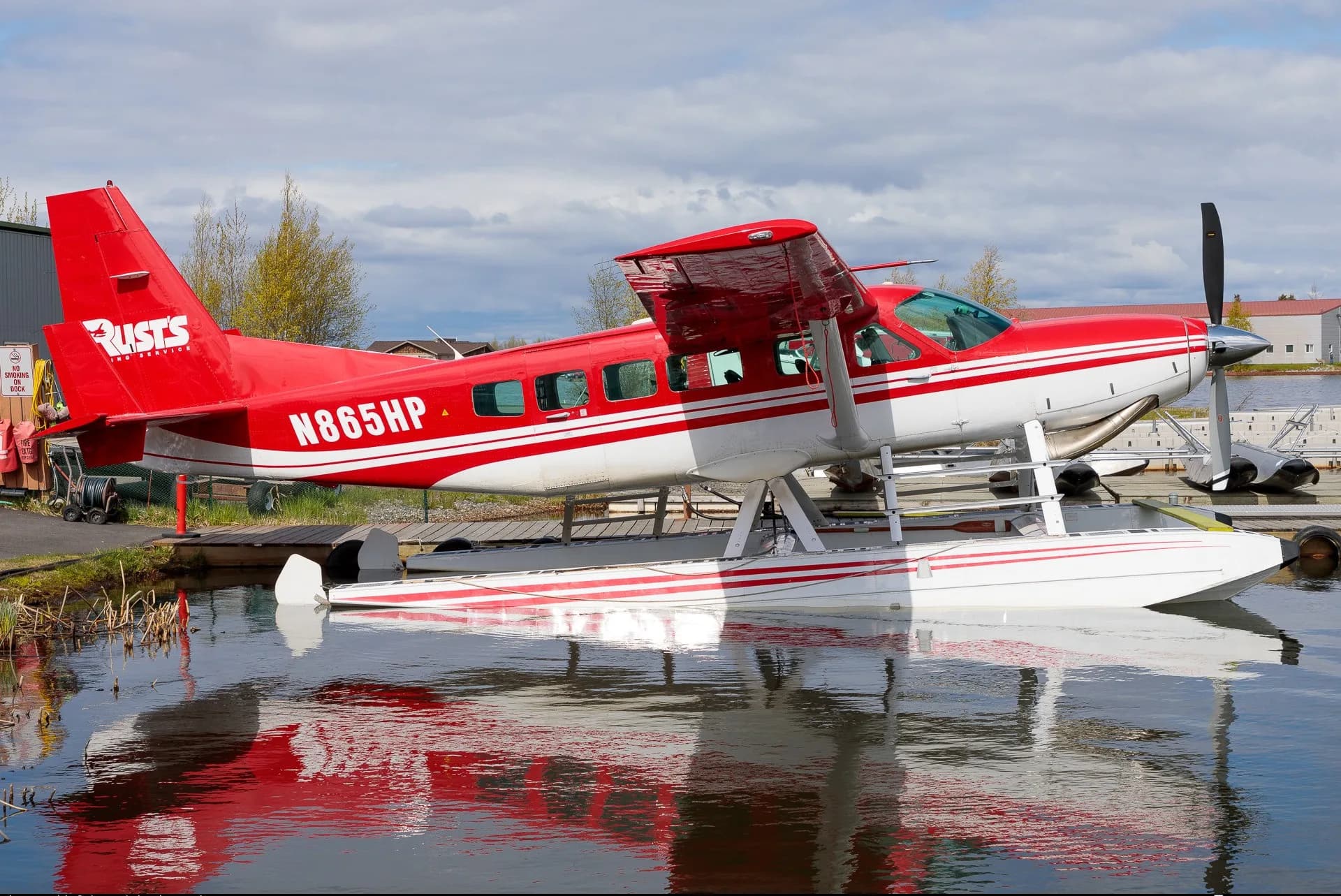 Red and white floatplane N865HP parked on a lake, reflected in the water.