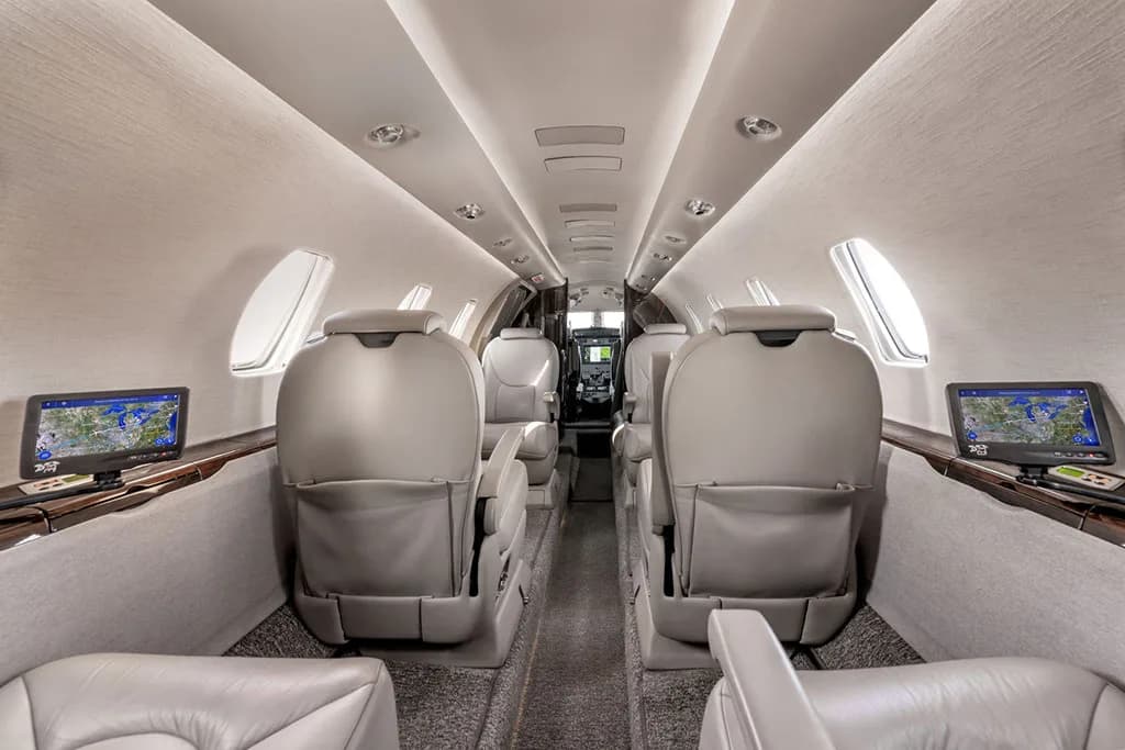 The aircraft cabin interior with light leather seats and individual screens mounted on the side panels.