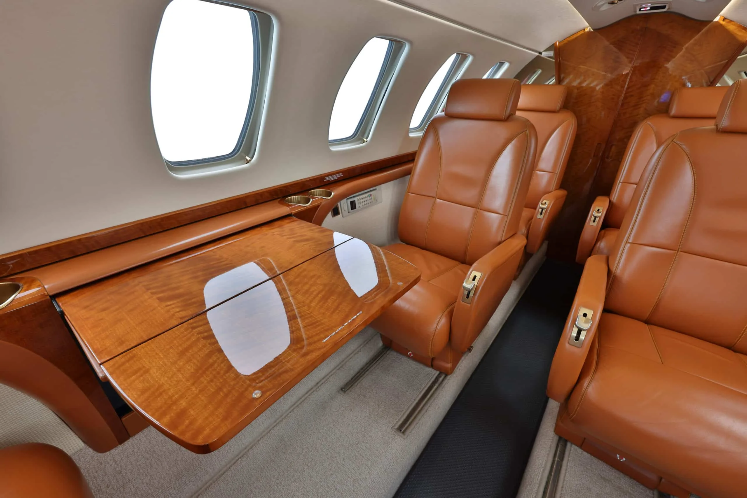 Side view of a private jet cabin showing tan leather seats and a polished wooden table.