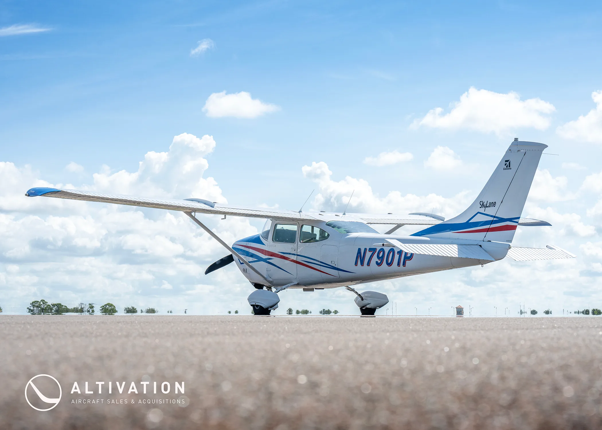A low-angle side view of a white Cessna 182 Skylane with blue and red stripes on a tarmac under a partly cloudy sky.