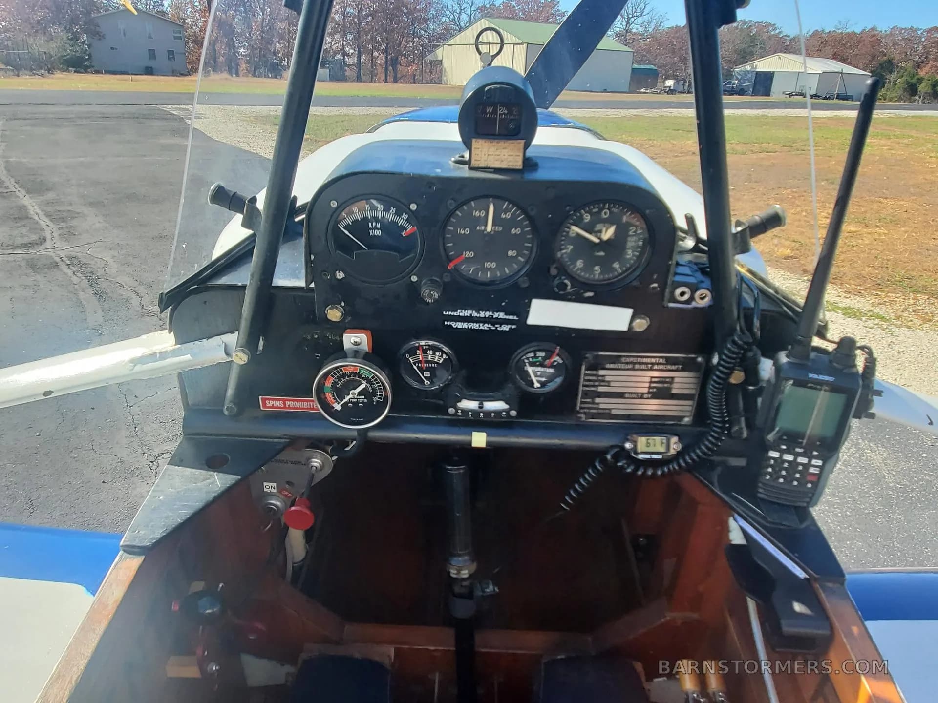 The cockpit of a small aircraft shows an instrument panel with gauges, a radio, and a wooden interior.