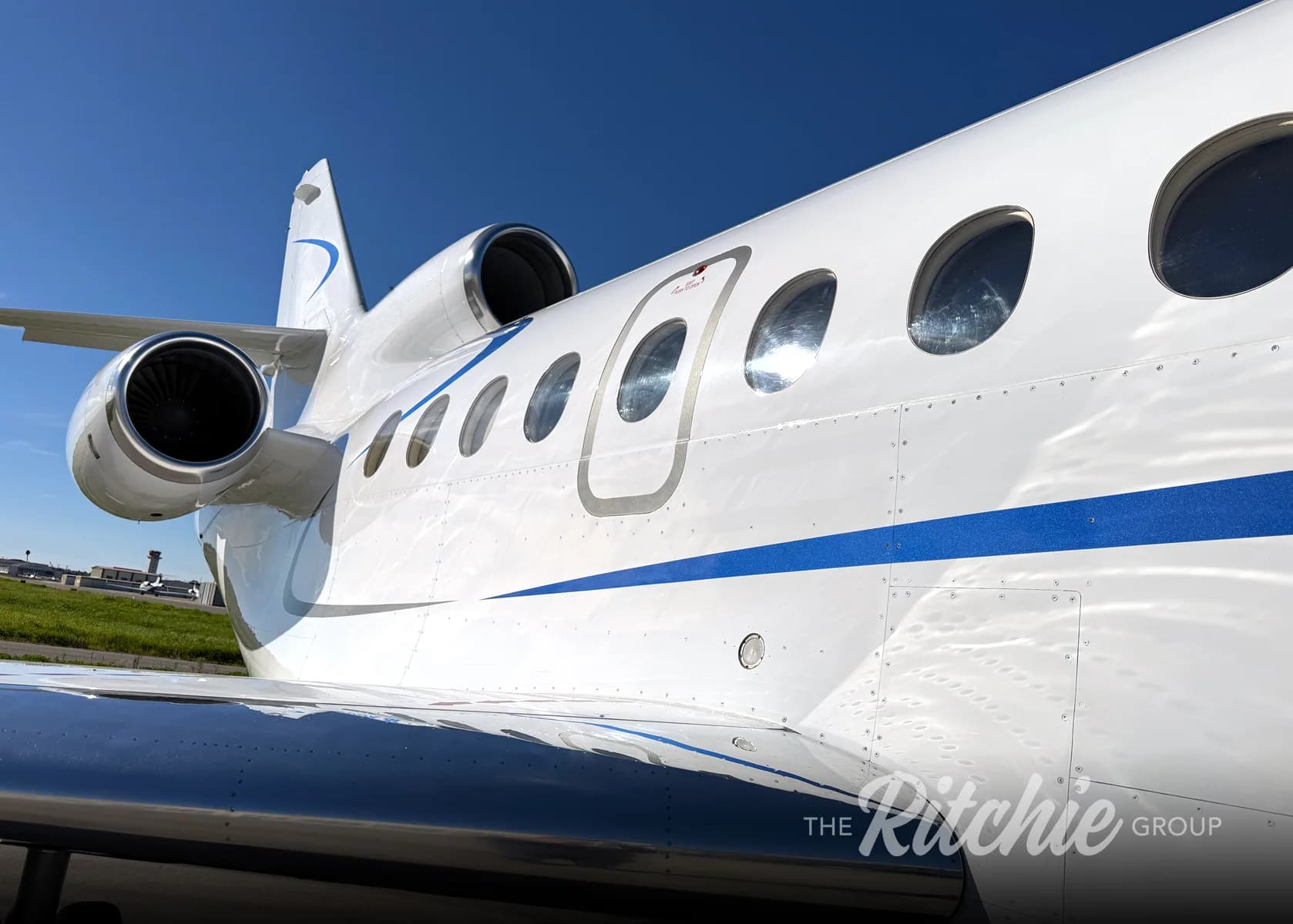A close-up view of the white business jet's fuselage, engine, and windows with blue stripe details.