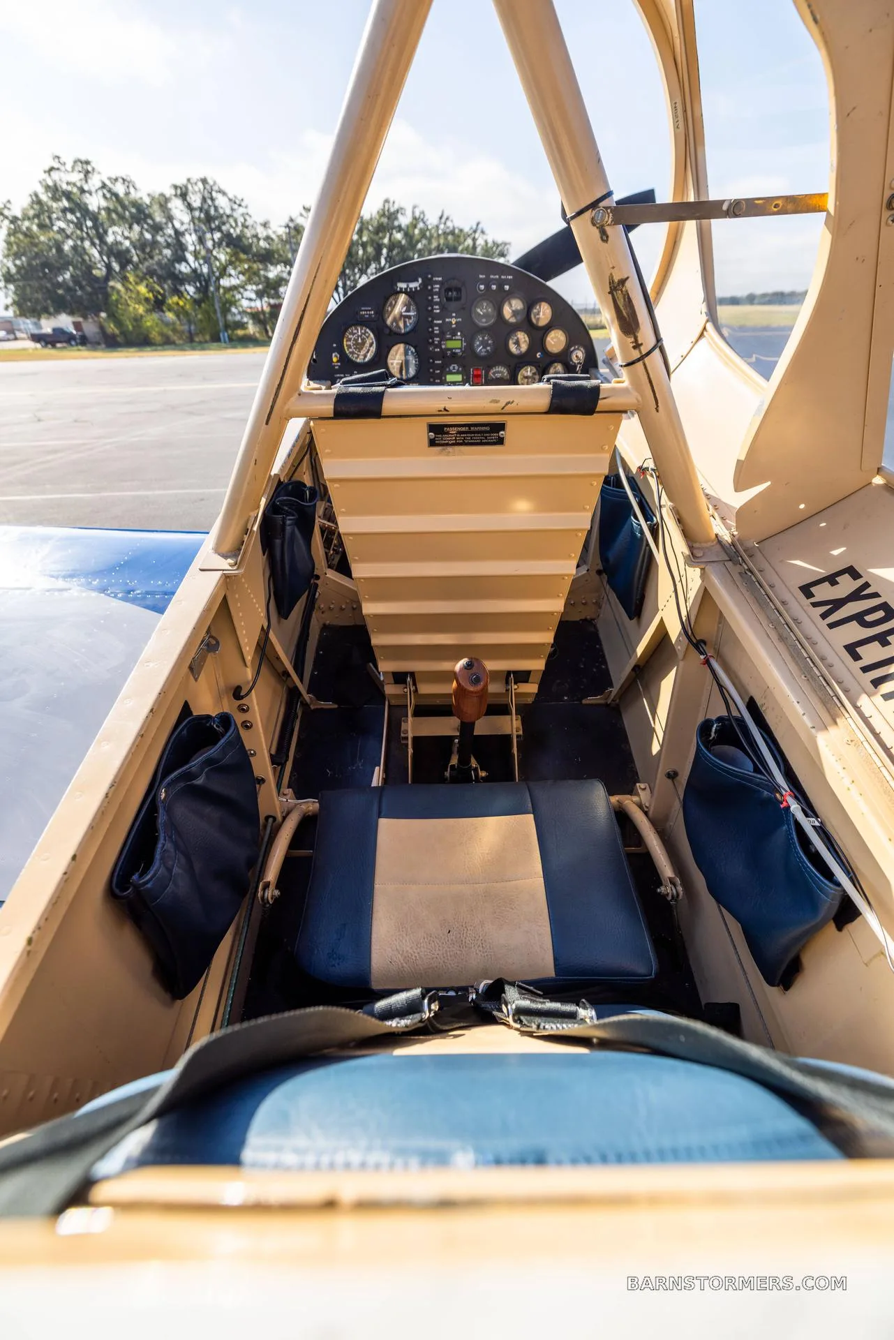 The interior of a single-seat aircraft cockpit, showing the blue and tan seat, control stick, and instrument panel.