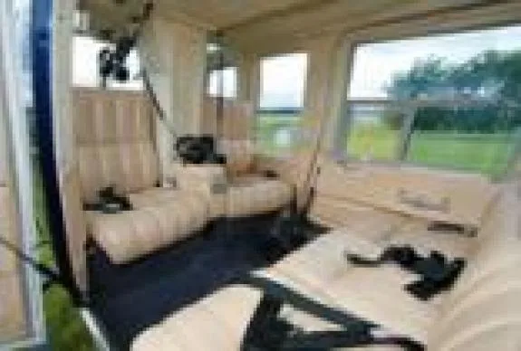 Interior view of a helicopter cabin with cream-colored seats and black seatbelts.