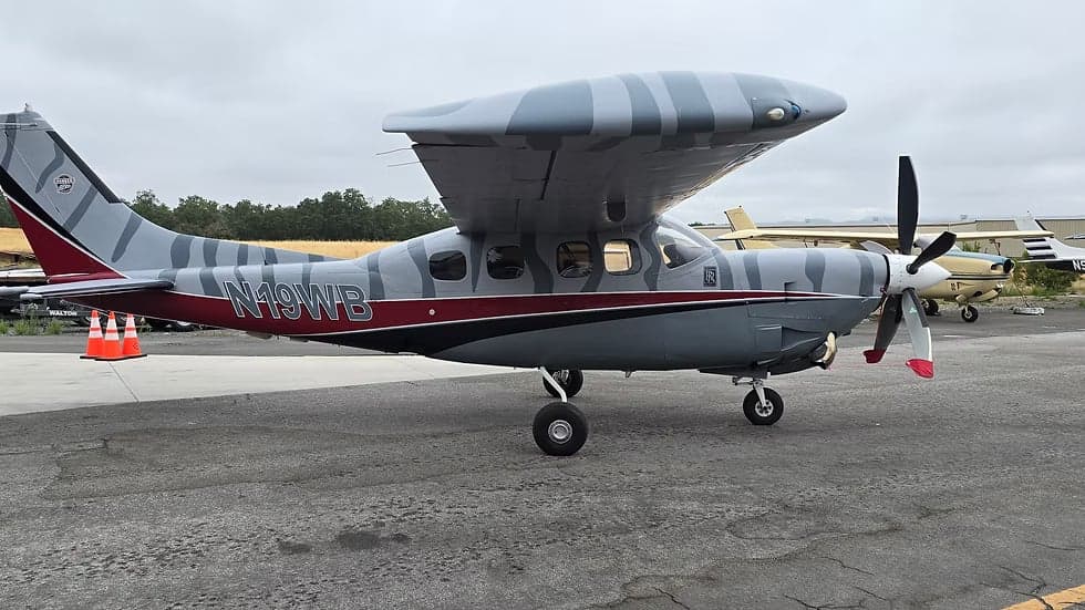 A Cessna Caravan, registration N19WB, parked on the tarmac with a unique gray and white striped paint scheme.