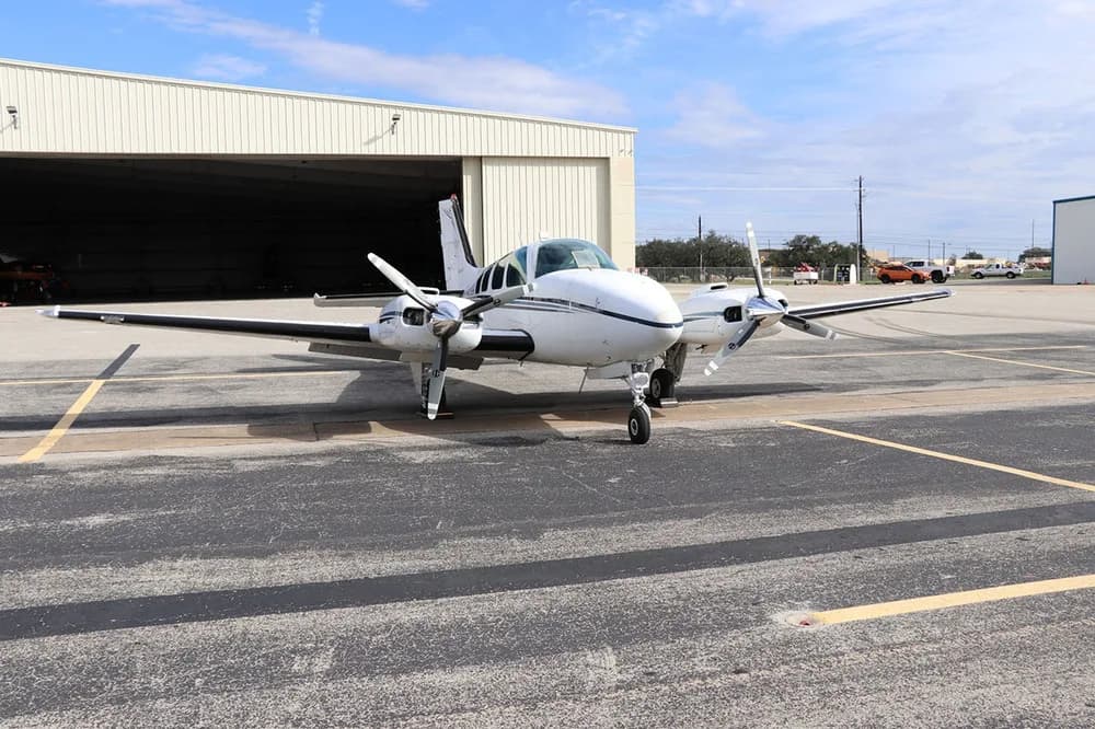 A front view of a white and black Beechcraft Baron 58 (N36TC) parked on an asphalt ramp in front of a hangar.