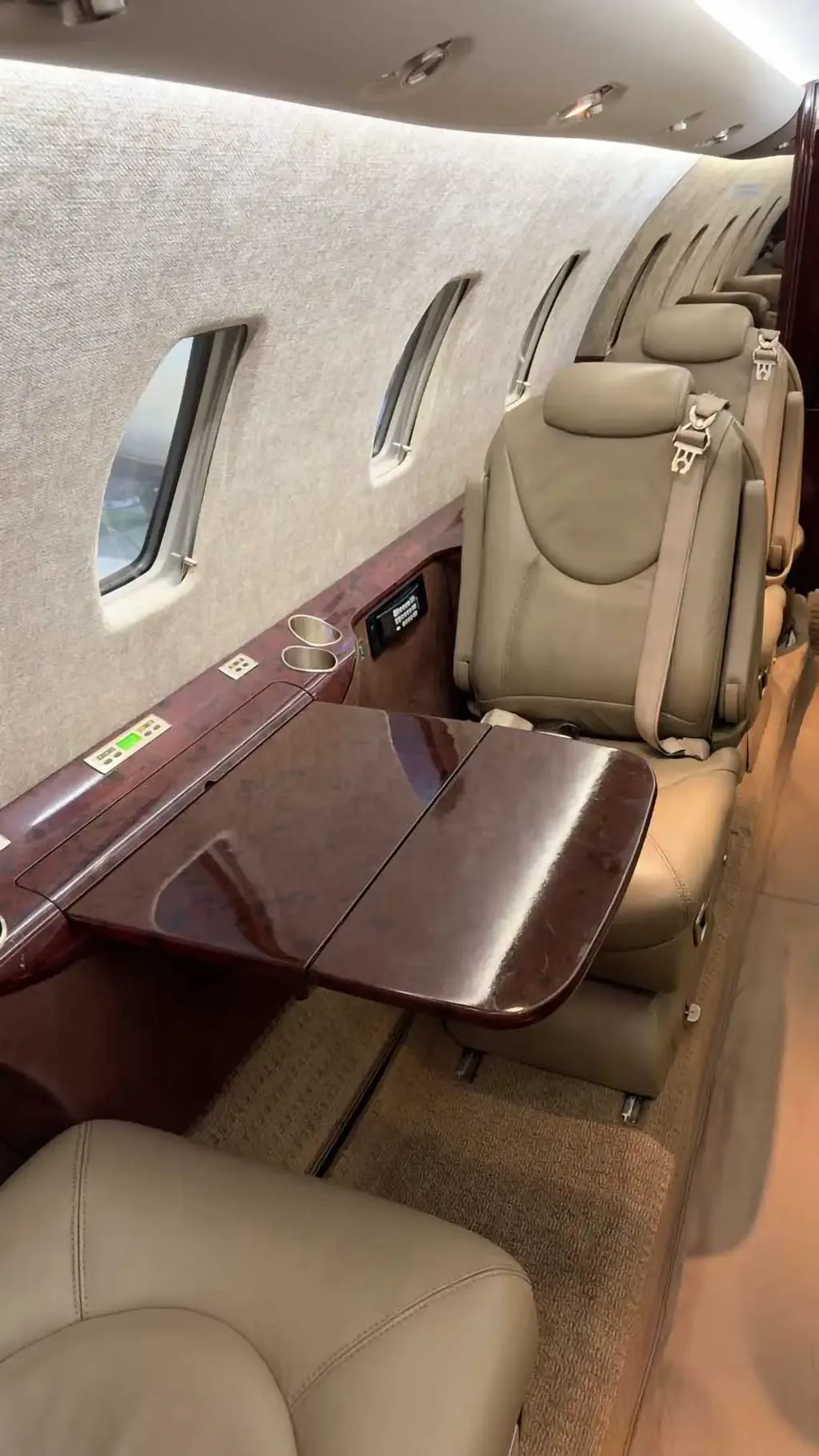 Close-up view of the aircraft cabin interior showing beige leather seats, a polished wooden side table, and windows.