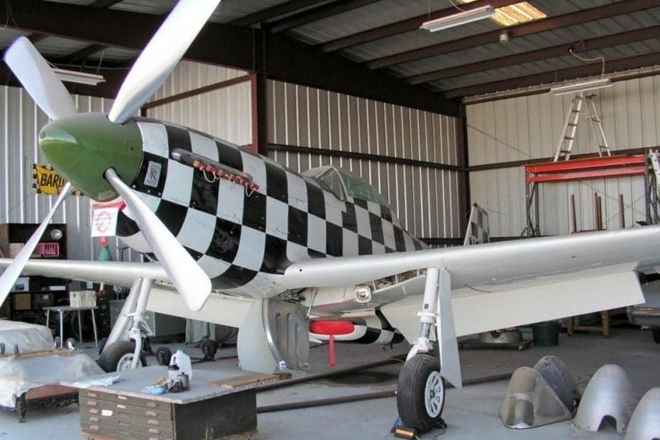 A P-51 Mustang with a black and white checkered paint scheme inside a hangar.
