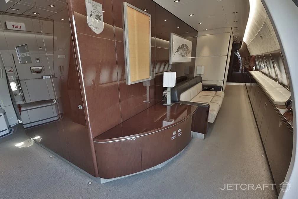 A luxurious aircraft cabin interior with dark wood paneling, a curved counter, and a long sofa.