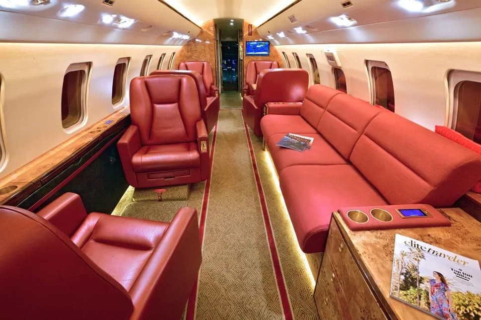 A spacious aircraft cabin interior with red leather seating, including a sofa and individual chairs, and wood accents.